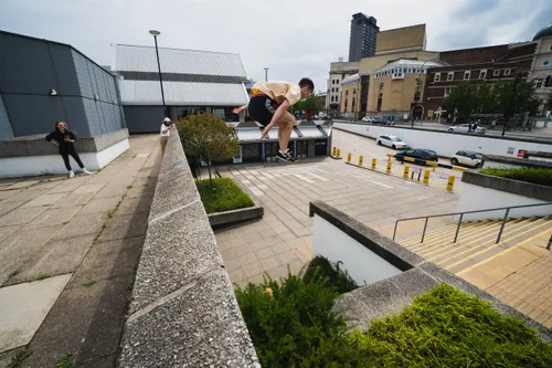 Arthur Gledhill-Franks vaulting over a rooftop wall in an urban plaza